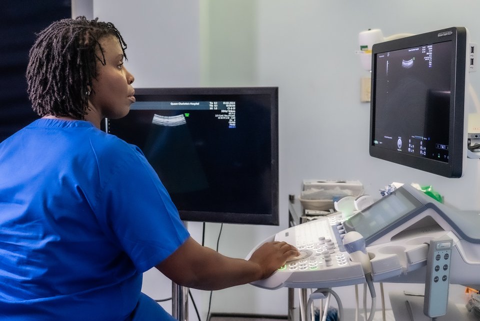 A female healthcare professional sits looking at screens on a sonography machine
