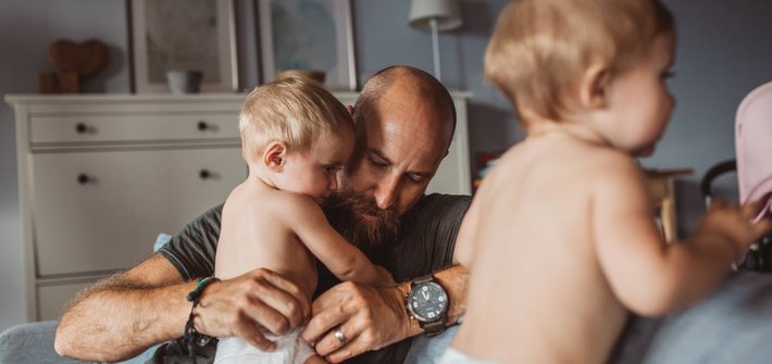 A man attends to the nappy of a baby in the background with another baby in the foreground