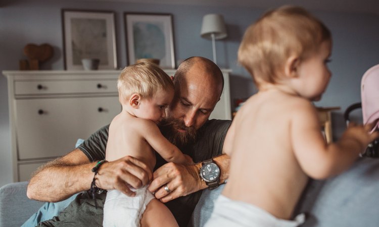 A man attends to the nappy of a baby in the background with another baby in the foreground