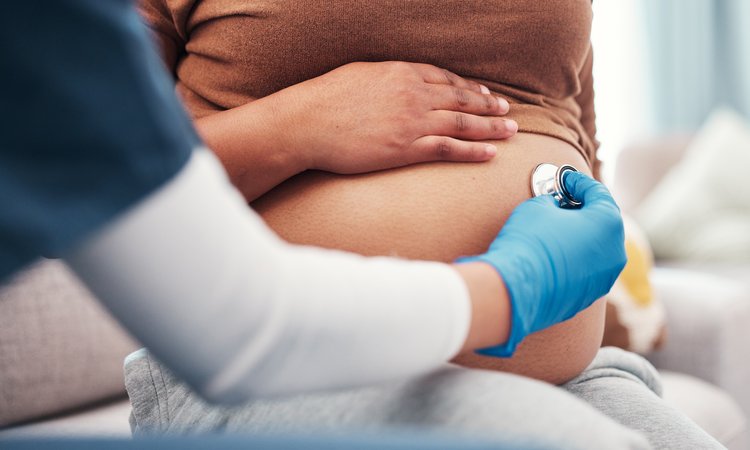 A closeup of a stethoscope being held to a pregnant belly