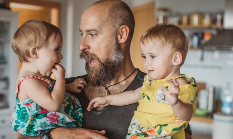 A man holds two toddlers in his arms as he makes a face at one of them