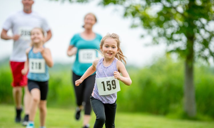 A young girl in the foreground runs towards the camera as a man, woman and child in the background chase after her
