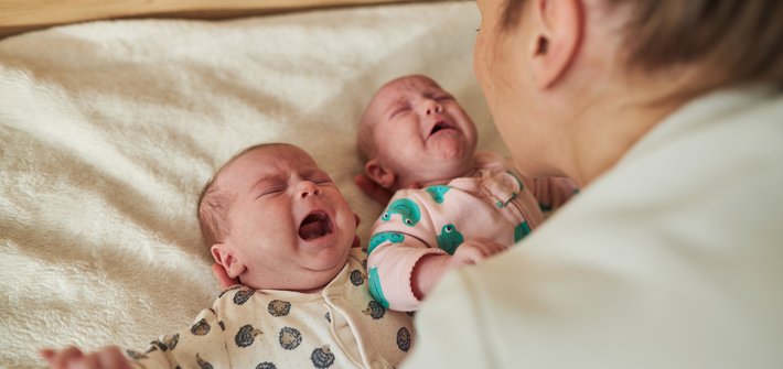 A woman leans over comforting crying twin babies