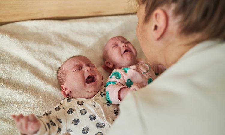 A woman leans over comforting crying twin babies