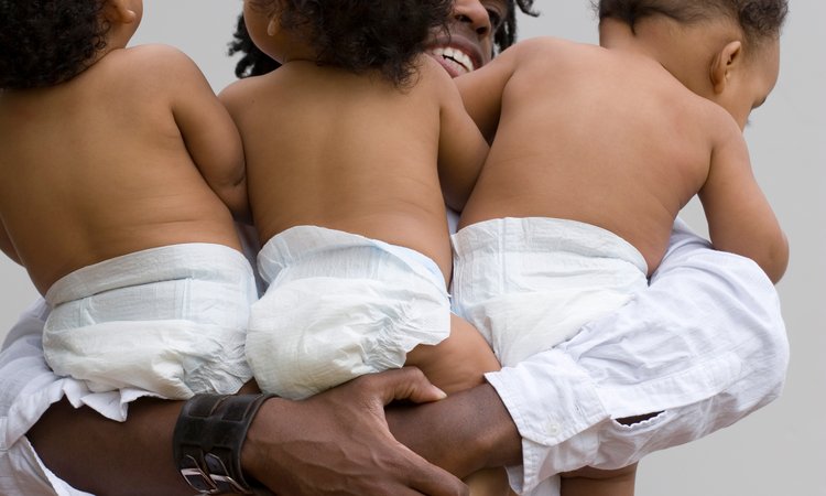 A closeup picture of a person's arms around triplet babies
