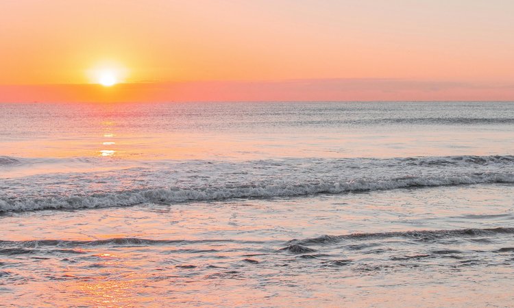A sunset in the distance with the ocean in the foreground