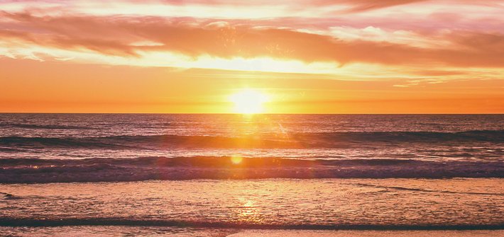 A sunset in the distance with waves rolling onto a beach in the foreground