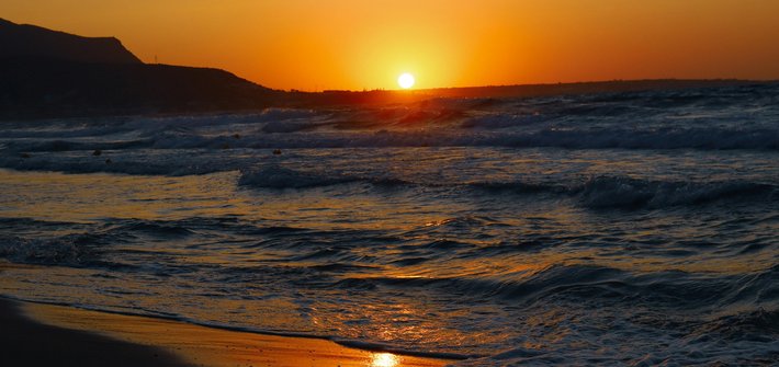 A sunset in the distance with waves rolling onto a beach in the foreground