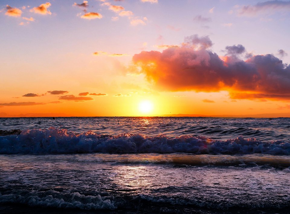 A sunset in the distance with waves rolling in the foreground