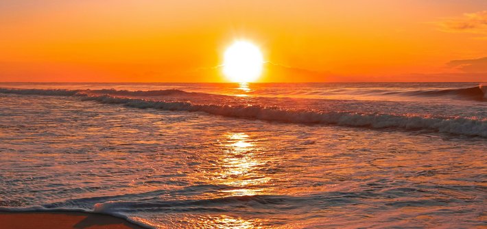 A sunset in the distance with waves rolling onto a beach in the foreground
