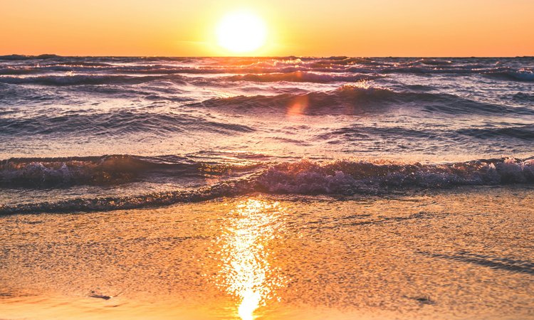 A sunset in the distance with waves rolling onto a beach in the foreground