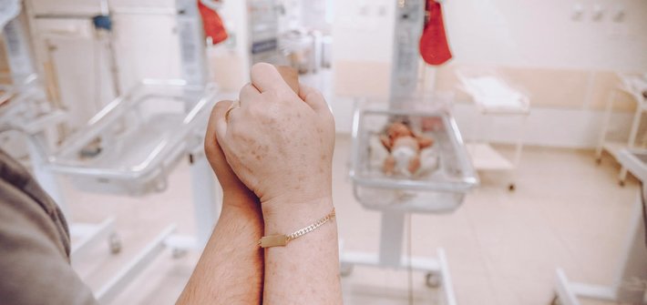 image of parents holding in hope overlooking one empty cot and one cot with a baby inside