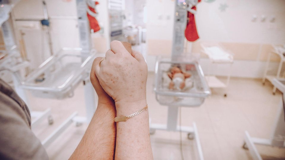 image of parents holding in hope overlooking one empty cot and one cot with a baby inside