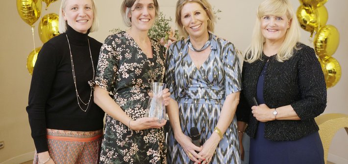 image of four women smiling with one being presented with an award