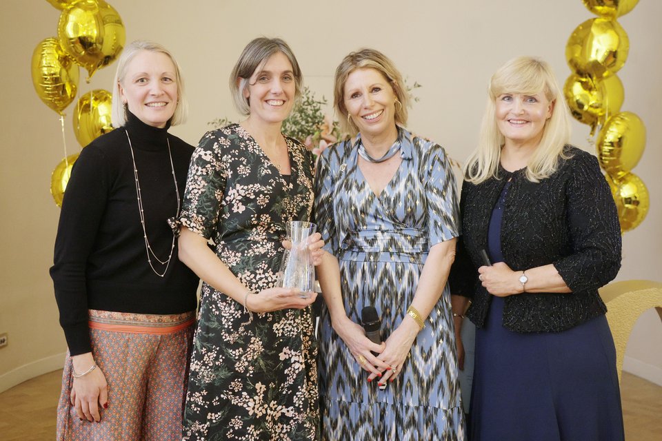 image of four women smiling with one being presented with an award
