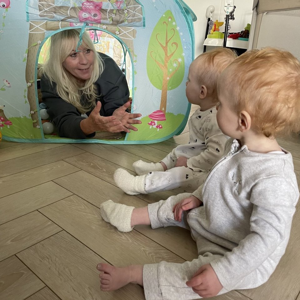 woman in a play tent offering a hug to a set of twins