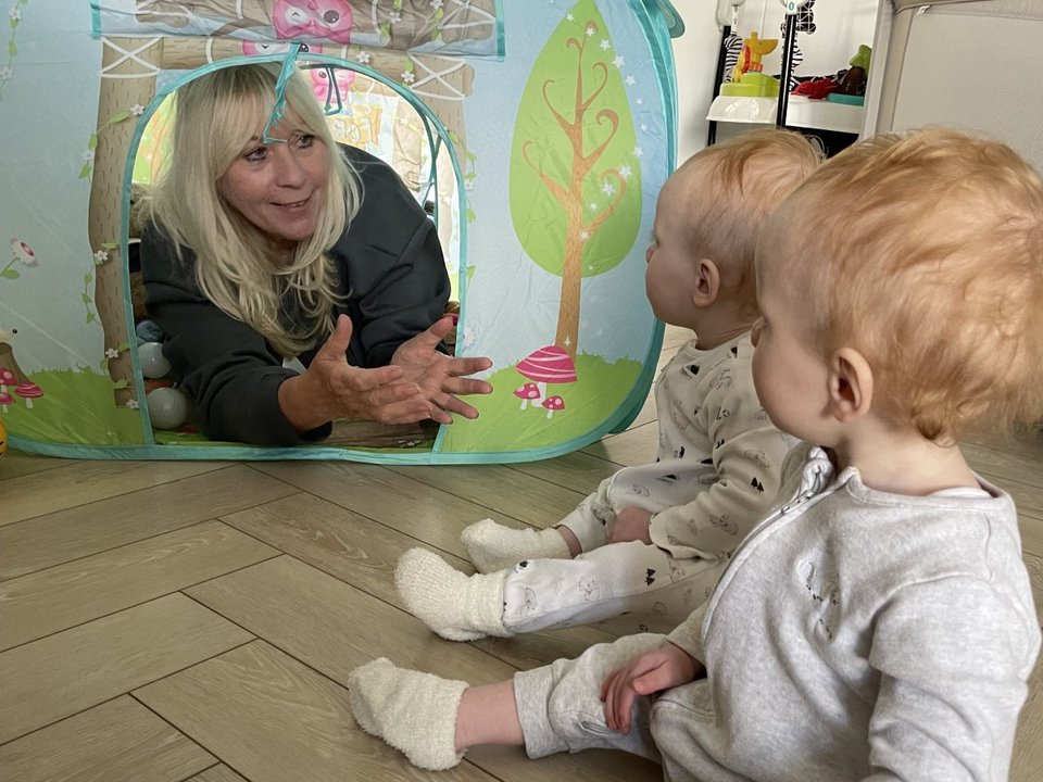 a grandmother in a play tent offering a hug to a set of twins