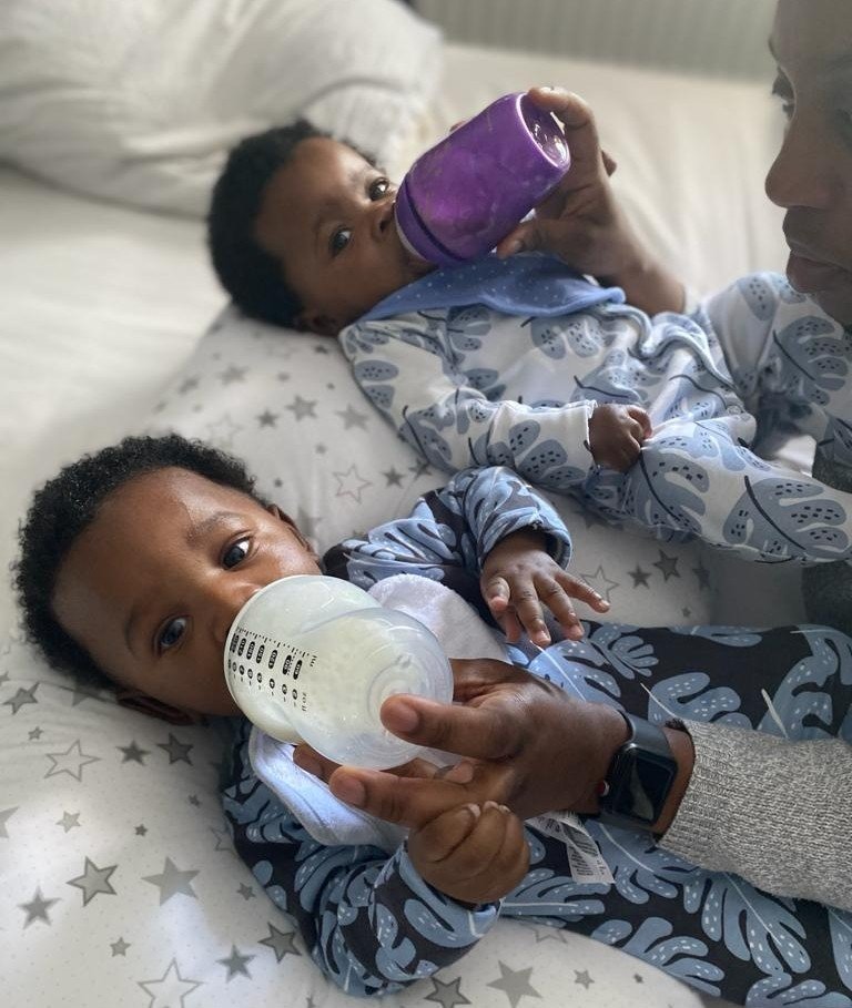 black woman tandem bottle feeding twin babies in bouncers