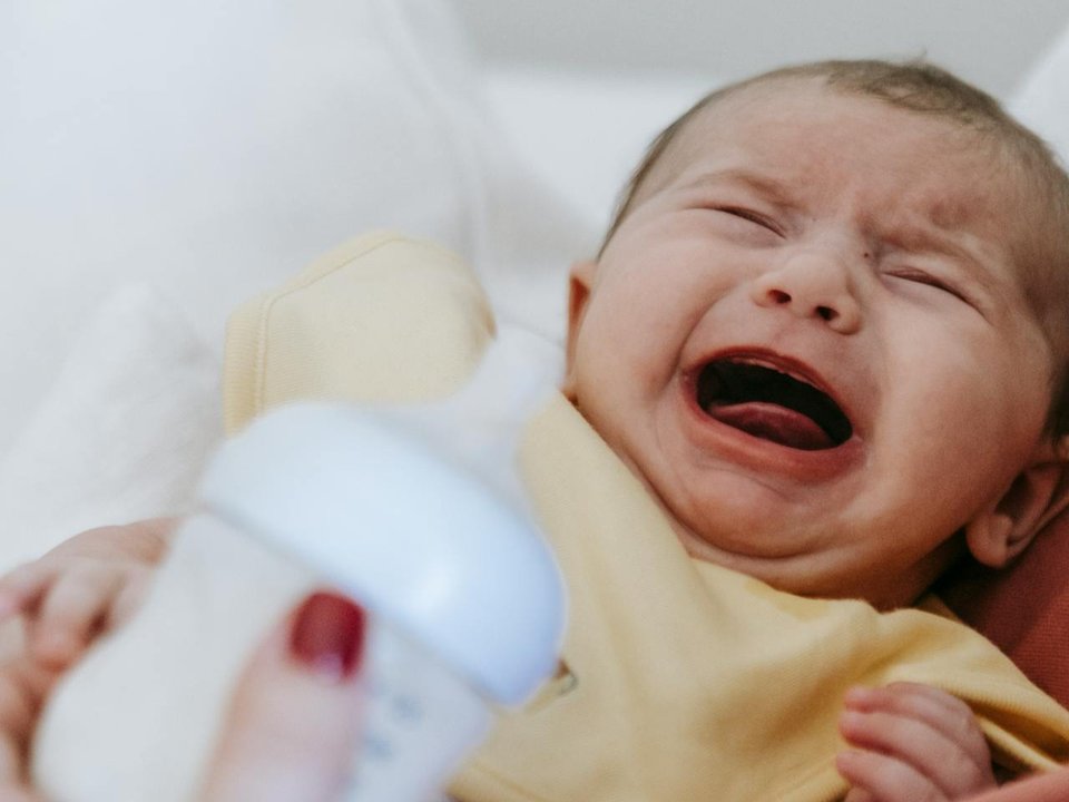 baby crying with a bottle of milk in the foreground