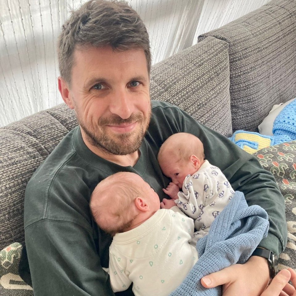 man smiling while holding twin babies