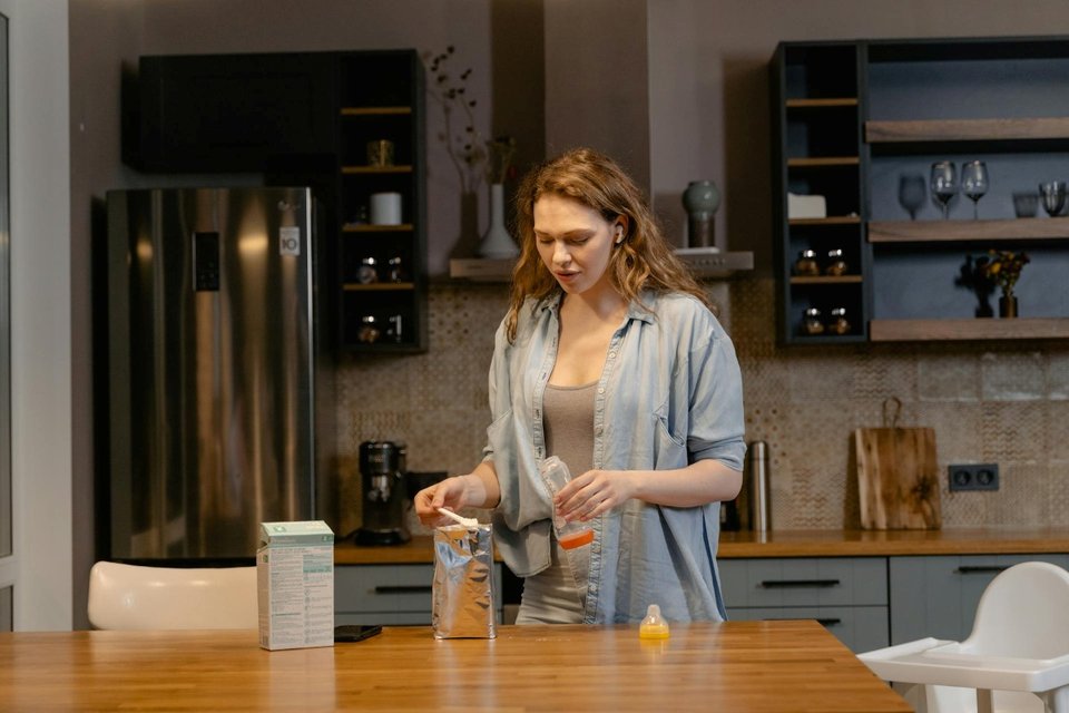 a woman holding a baby bottle preparing milk formula in a kitchen