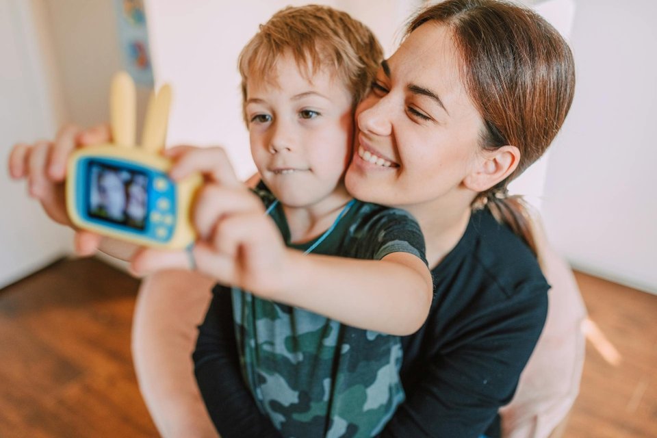 child taking a selfie with his mother using a children's camera