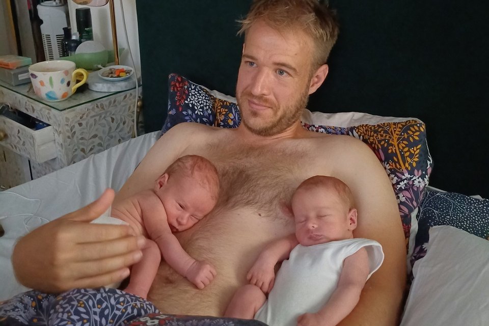 man lying in bed holding sleeping twin babies