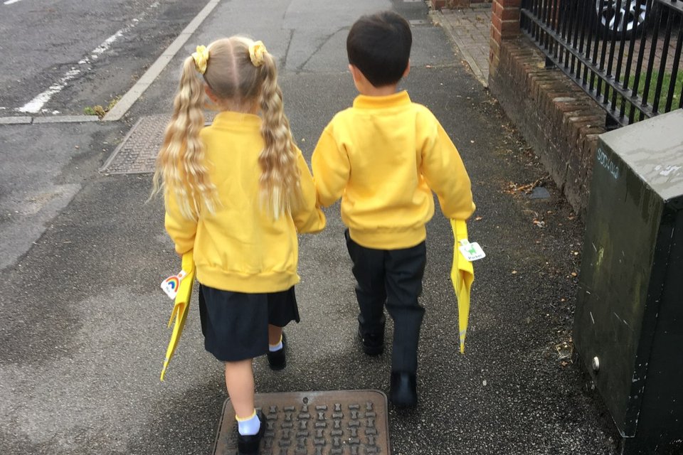 a boy and a girl in school uniform holding hands walking on the pavement