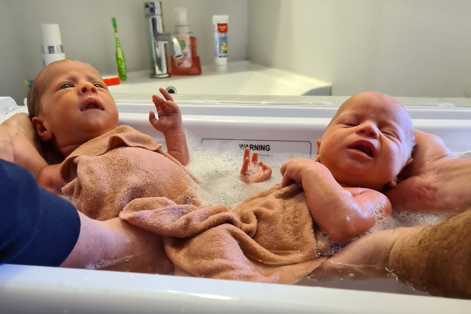 twin babies being bathed in a baby bath by two parents