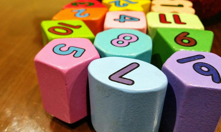 Wooden blocks in different colours with numbers written on them lay on a wooden floor