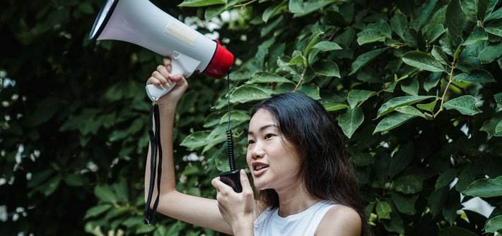 A woman holds a megaphone in the air whilst speaking into a receiver