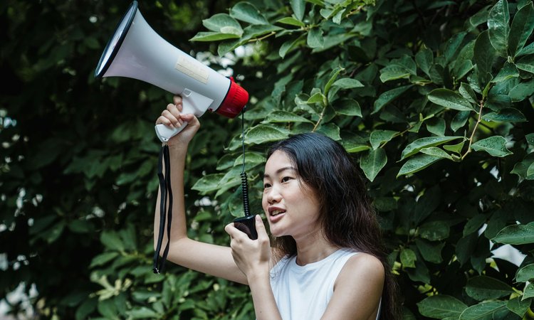 A woman holds a megaphone in the air whilst speaking into a receiver