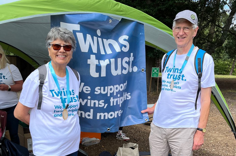 Judi and Howard Linney stand in Twins Trust t-shirts with a Twins Trust banner between them
