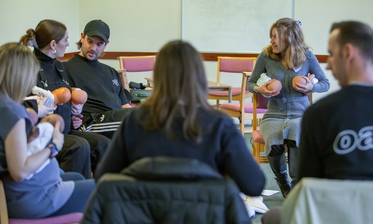 A group of people sit in a circle practicing feeding with baby dummies