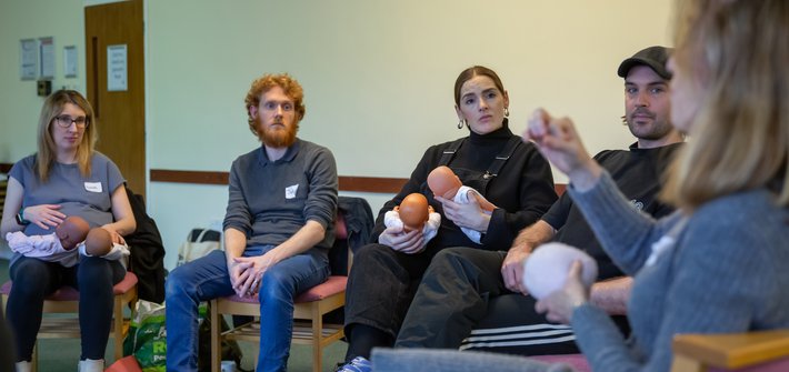 Two couples sit listening to a person in the foreground speaking