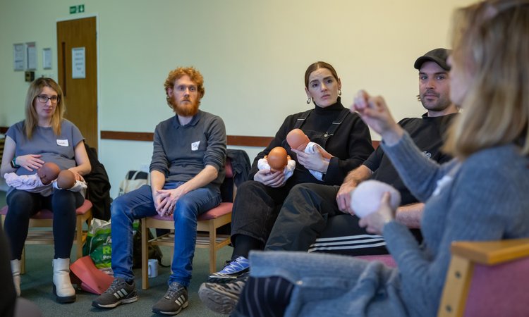 Two couples sit listening to a person in the foreground speaking