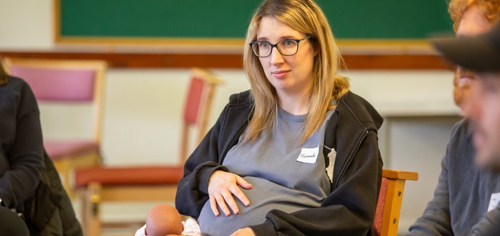 A woman sits holding her pregnant belly with twin baby dummies on her lap