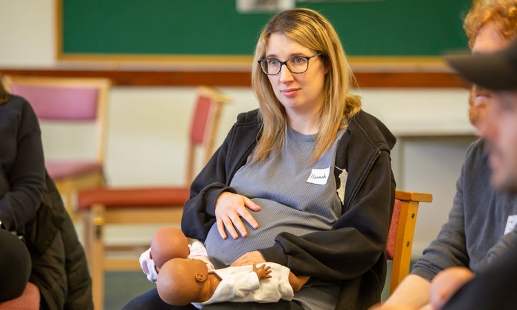A woman sits holding her pregnant belly with twin baby dummies on her lap