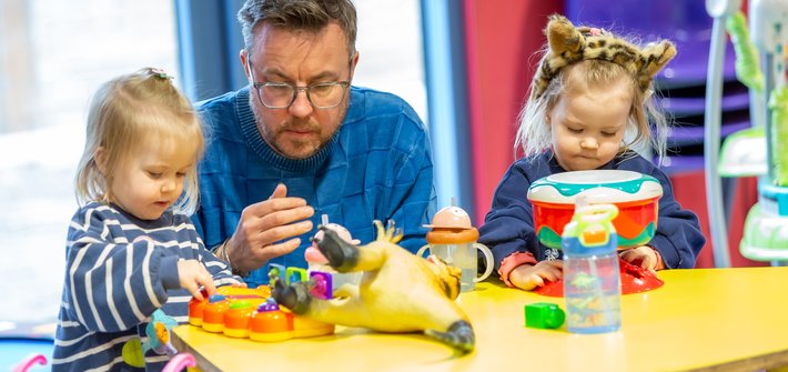 A man helps twin girls play on a table
