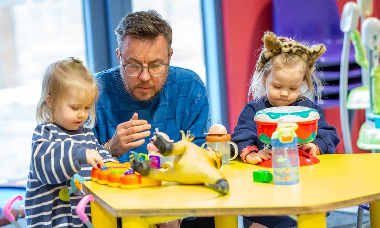 A man helps twin girls play on a table
