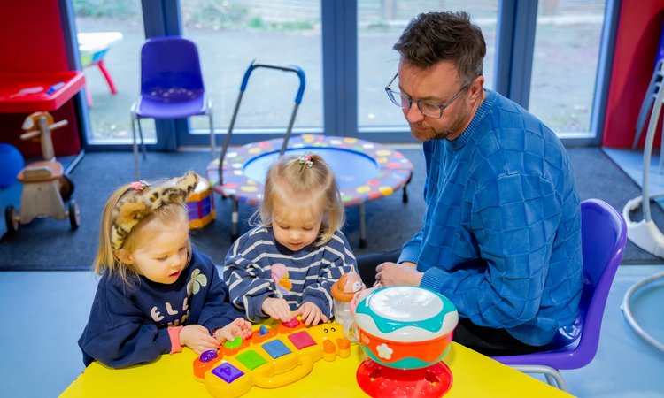 A man sits at a table with young twin girls playing with toys
