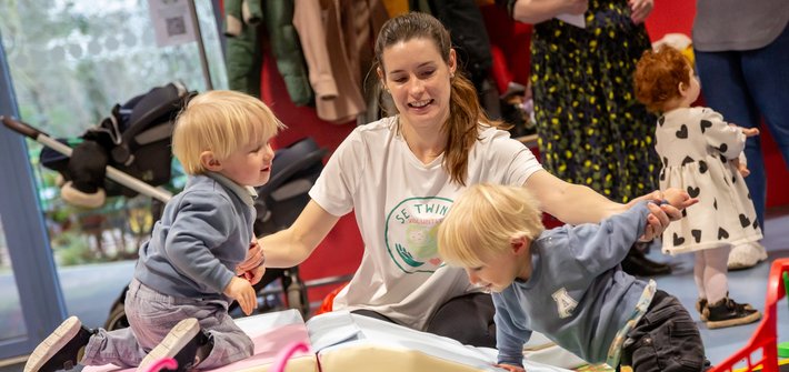 A woman supports twin boys climbing on soft shapes