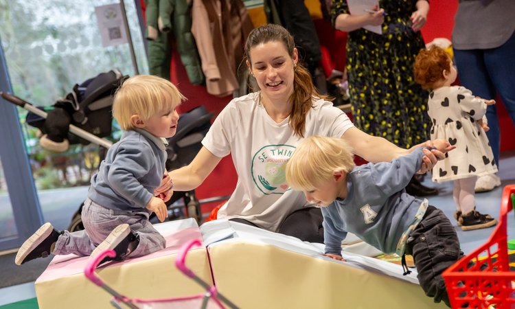 A woman supports twin boys climbing on soft shapes