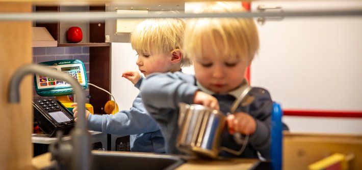 Twin toddlers play in a toy kitchen
