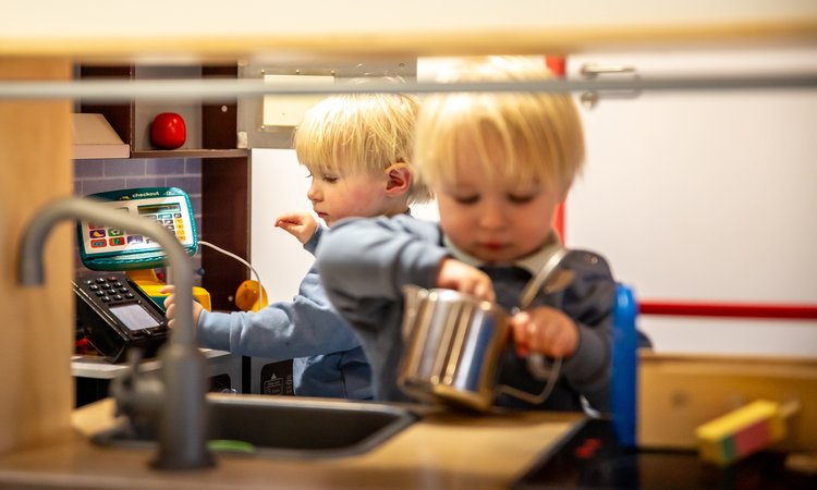 Twin toddlers play in a toy kitchen