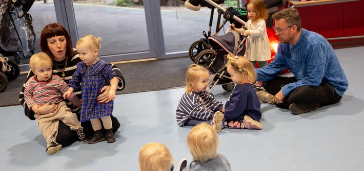 A woman sits on the floor with twins on the left of the image, a man with twins on the right and a set of twins sit in the foreground looking at them