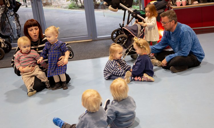 A woman sits on the floor with twins on the left of the image, a man with twins on the right and a set of twins sit in the foreground looking at them