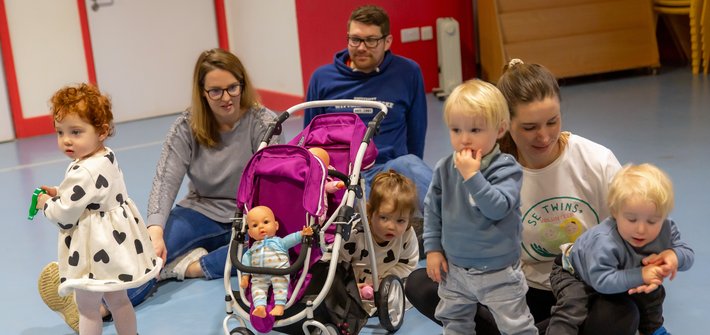 Two woman and a man sit on the floor as two sets of twins play around them