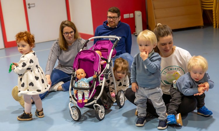 Two woman and a man sit on the floor as two sets of twins play around them