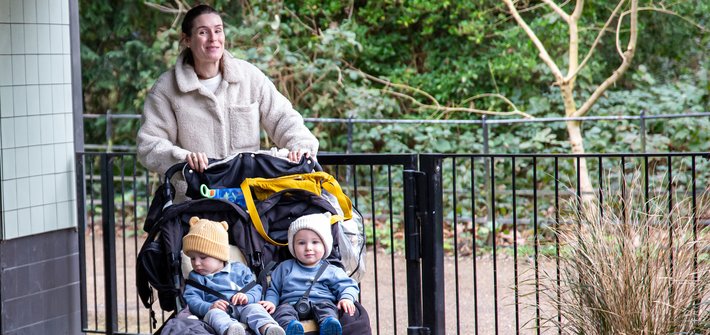 A woman pushes a twin pushchair with twin toddlers sitting in it